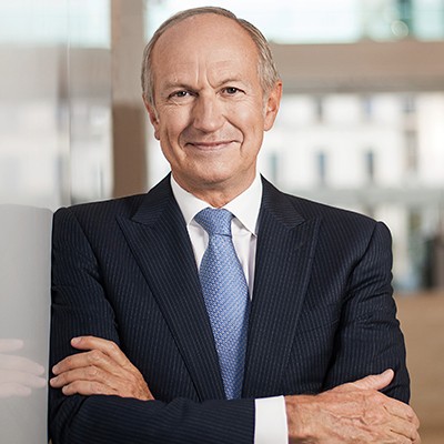 Professional businessman in navy pinstripe suit and blue tie with arms crossed, smiling at camera in modern office setting